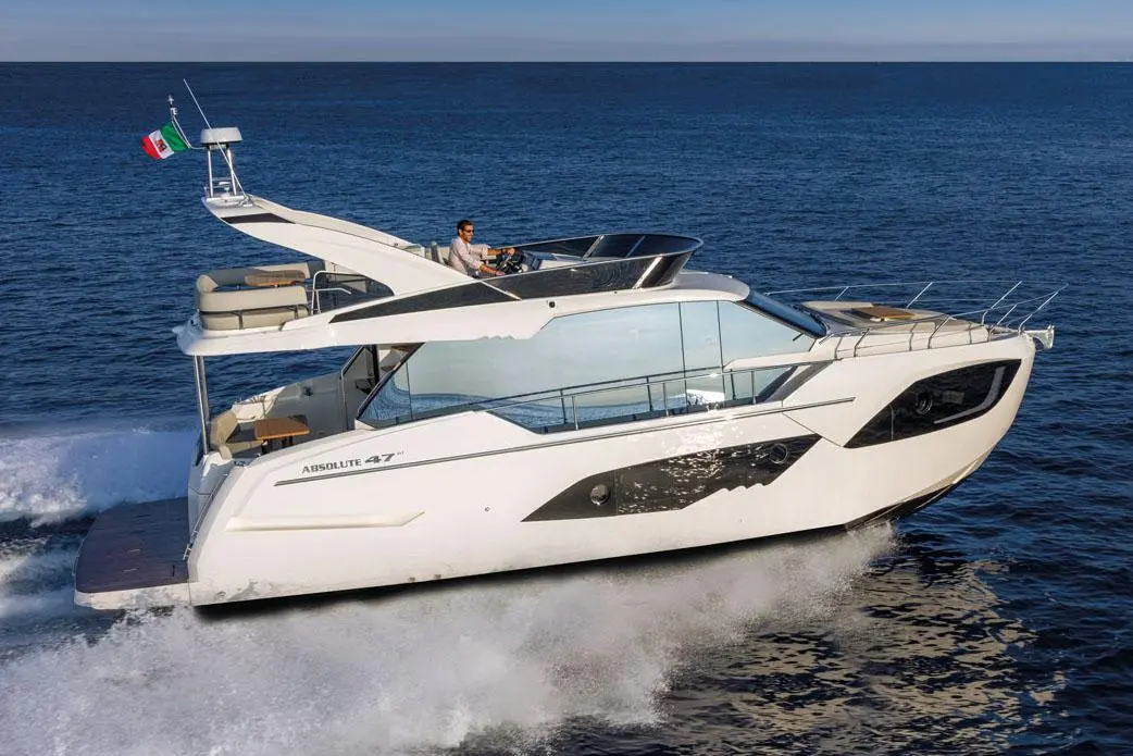 A white Absolute 47 yacht sails through blue waters with a man at the helm, displaying an Italian flag.